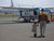 The back picture of the tan brown leather backpack on a woman's back as her toddler son is running towards her in Africa.