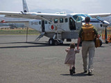 The back picture of the tan brown leather backpack on a woman's back as her toddler son is running towards her in Africa.