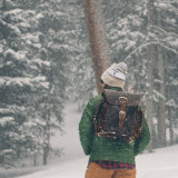 This  is a man lost in the snow wearing a dark brown leather backpack.