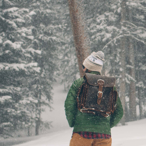 This  is a man lost in the snow wearing a dark brown leather backpack.