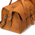 This is a tan brown leather duffle bag that has three straps to close it and has two round handles from the end.