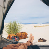This is a tan brown leather duffle bag outside of a tent in the sand.