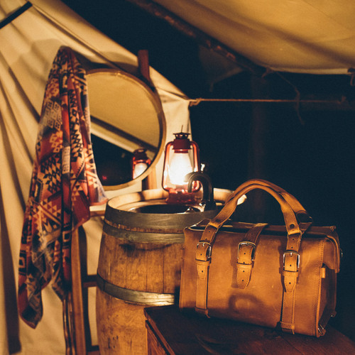 This is a tan brown leather duffle bag at a campsite.