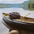 This is a dark brown leather duffle bag with three straps on the front of a canoe on a lake.