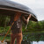 This is a dark brown leather duffle bag with three straps on a man's back as a backpack while he carries a canoe.