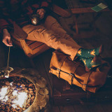 This is a tan brown leather duffle bag being used as a camping footstool.full of overnight travel gear.