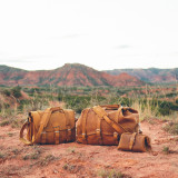 This is a tan brown leather duffle bag with three straps on front to hold overnight travel gear along with a doctor's overnight duffle to compare sizes.