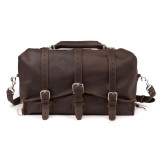 This is a dark brown leather duffle bag with three straps on the front and it is facing the camera. It has a travel overnight handle on top.