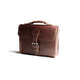 This is the front side of a red brown leather satchel with a front pocket angled.