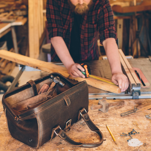 This dark brown leather doctor's leather tool bag is in a woodshop.