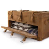 This is a leather trunk that will be a vintage antique one day in a museum. This is the front door of it that is open and angled. It is a tan brown steamer trunk that was old time luggage back in the day on trains and ships.