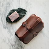 This is a red brown leather toiletry bag on the top side on snow.