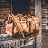 Here is the tobacco deep pocket duffle bag on the steps in front of a cabin. Made by Saddleback