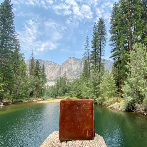 Tan large bifold leather wallet outdoors in front of a lake and tree. Made by Saddleback